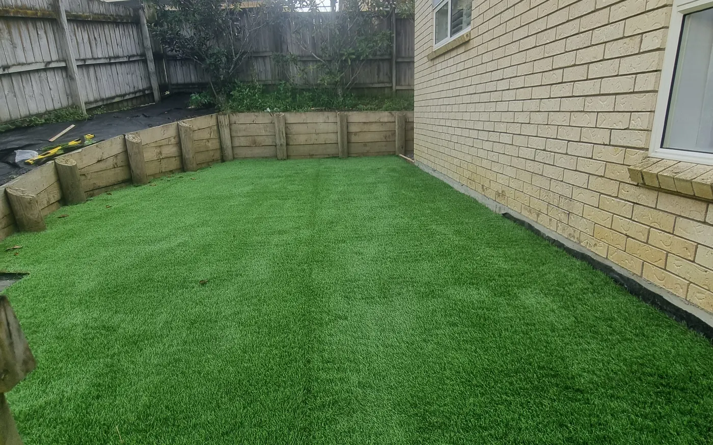 Artificial turf laid inside a timber-edged garden bed against a fence